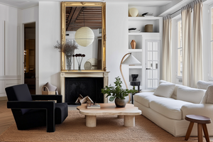Refined minimalist living room with a travertine coffee table, boucle sofa, antique gold mirror, and sculptural accents, showcasing the Atelier Residence aesthetic.