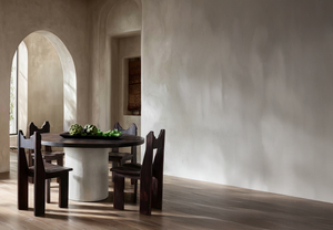 Brutalist-inspired dining space with arched architecture, solid timber chairs, and a pedestal table, emphasising strong geometry, natural materials, and emotionally grounding interiors.