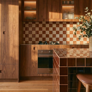 Warm timber kitchen with checkerboard tiled splashback, tiled island bench, wooden cabinetry, and natural light.
