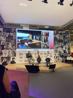 People on a stage with a large screen displaying images in a room with a collage wall.