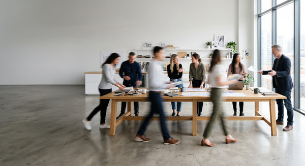 Group of people working together at a long wooden table in a modern office setting.